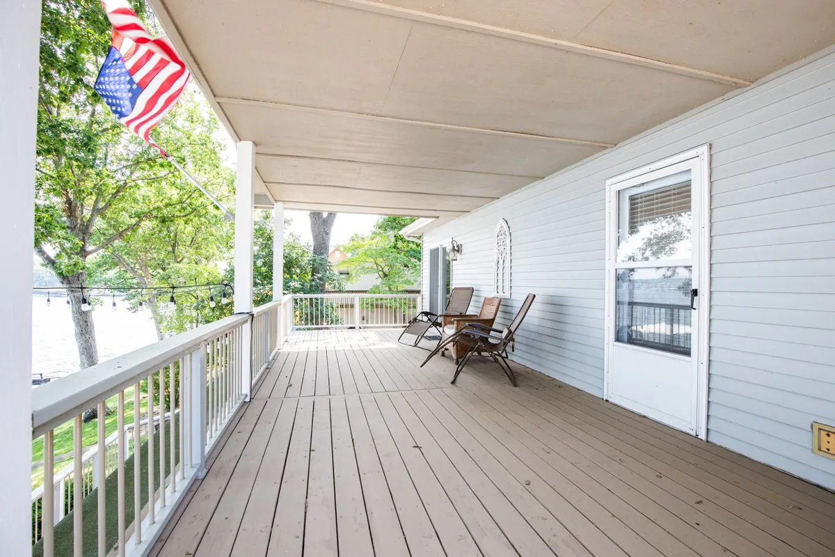 A peaceful porch with classic rocking chairs, overlooking the water and shaded by trees. The American flag and relaxing seating arrangement evoke a welcoming, homey atmosphere perfect for unwinding after an outdoor adventure with your pet.