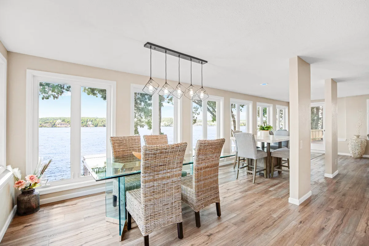 A serene dining area featuring a glass dining table surrounded by woven chairs, all set before expansive windows that overlook the water. The scene is bright and welcoming, inviting guests to savor meals together while taking in the lake view.