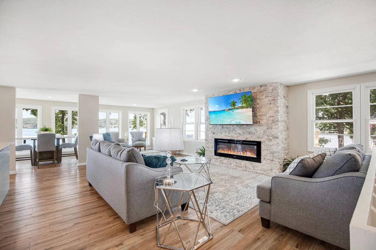 An open living and dining space with a modern fireplace, large TV, comfortable sofas, and a dining area that enjoys views from large windows. The setting is designed for relaxation, entertainment, and scenic enjoyment.