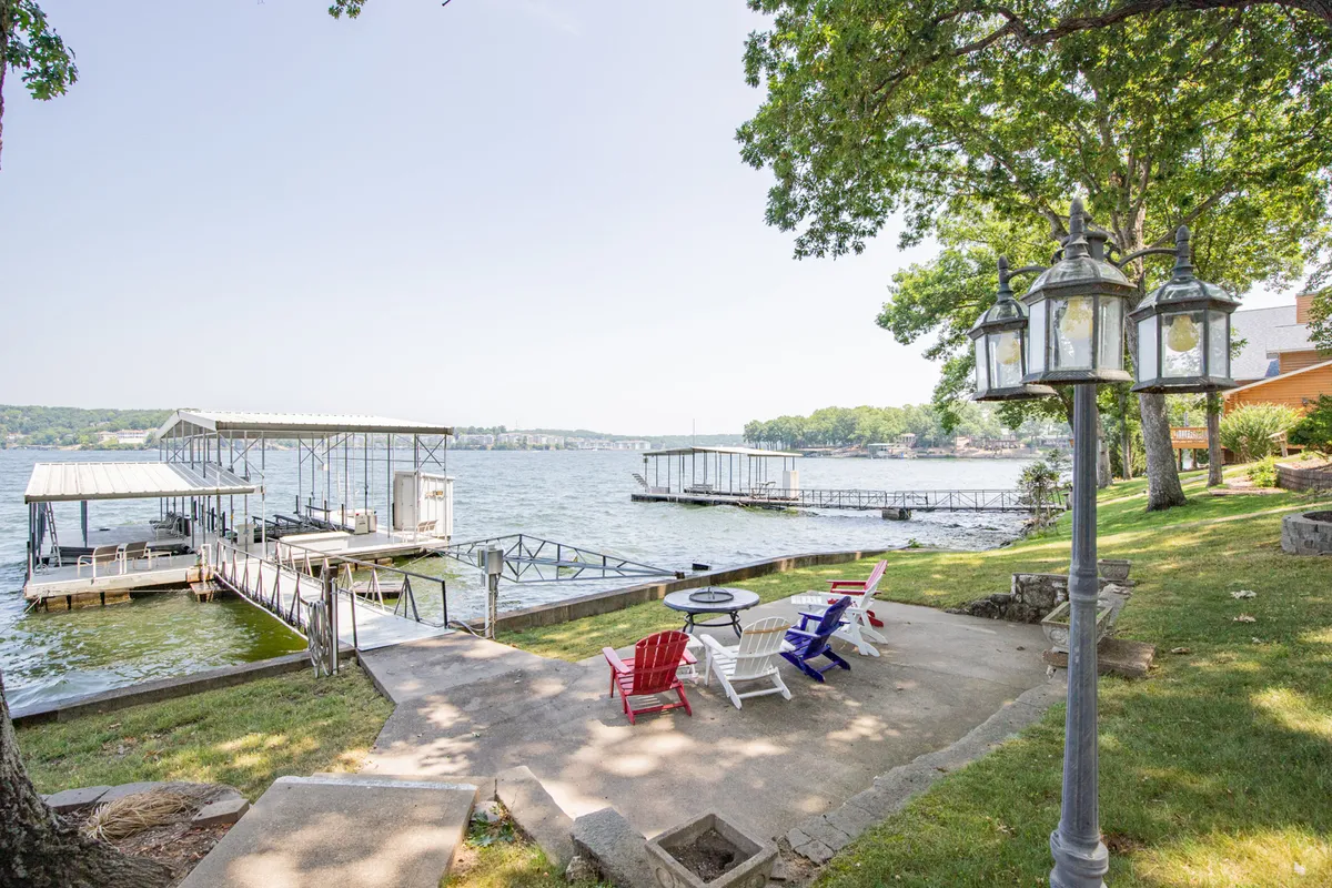 This image captures a peaceful waterfront scene featuring a private dock, fire pit surrounded by lawn chairs, and expansive lake views. The setting is perfect for both daytime relaxation and evening gatherings by the fire.