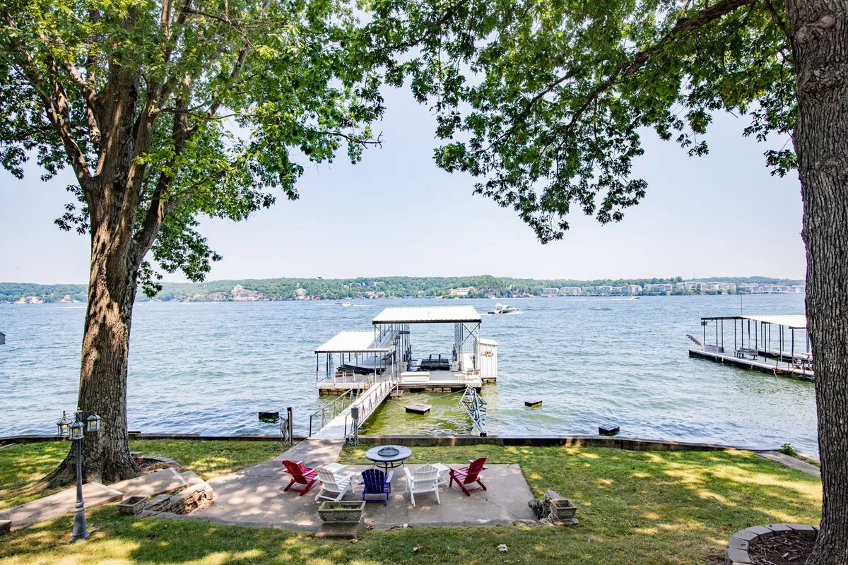 The image showcases a sweeping lakeside scene at sunset, featuring a private dock that extends over tranquil waters, surrounded by comfortable Adirondack chairs and a crackling fire pit. The setting invites relaxation and togetherness, with vibrant sky colors reflecting on the lake, perfect for family gatherings or enjoying quiet moments by the shore.