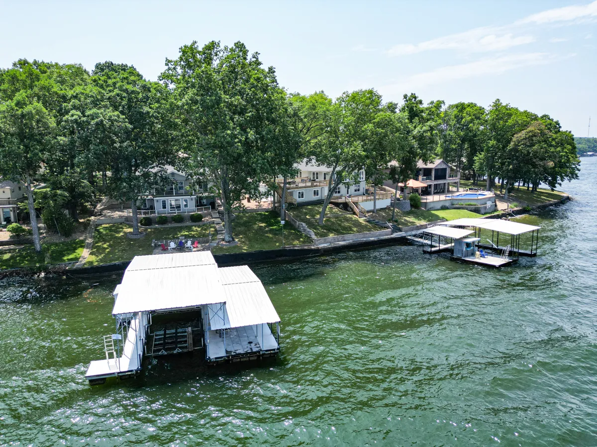 This image shows two lakefront homes nestled among lush trees, each with its own boathouse and direct access to the water. The spacious arrangement between the properties hints at multiple families or groups being able to enjoy their own space while sharing the lakeside setting. The scene conveys tranquility and ample room for gathering or spreading out.