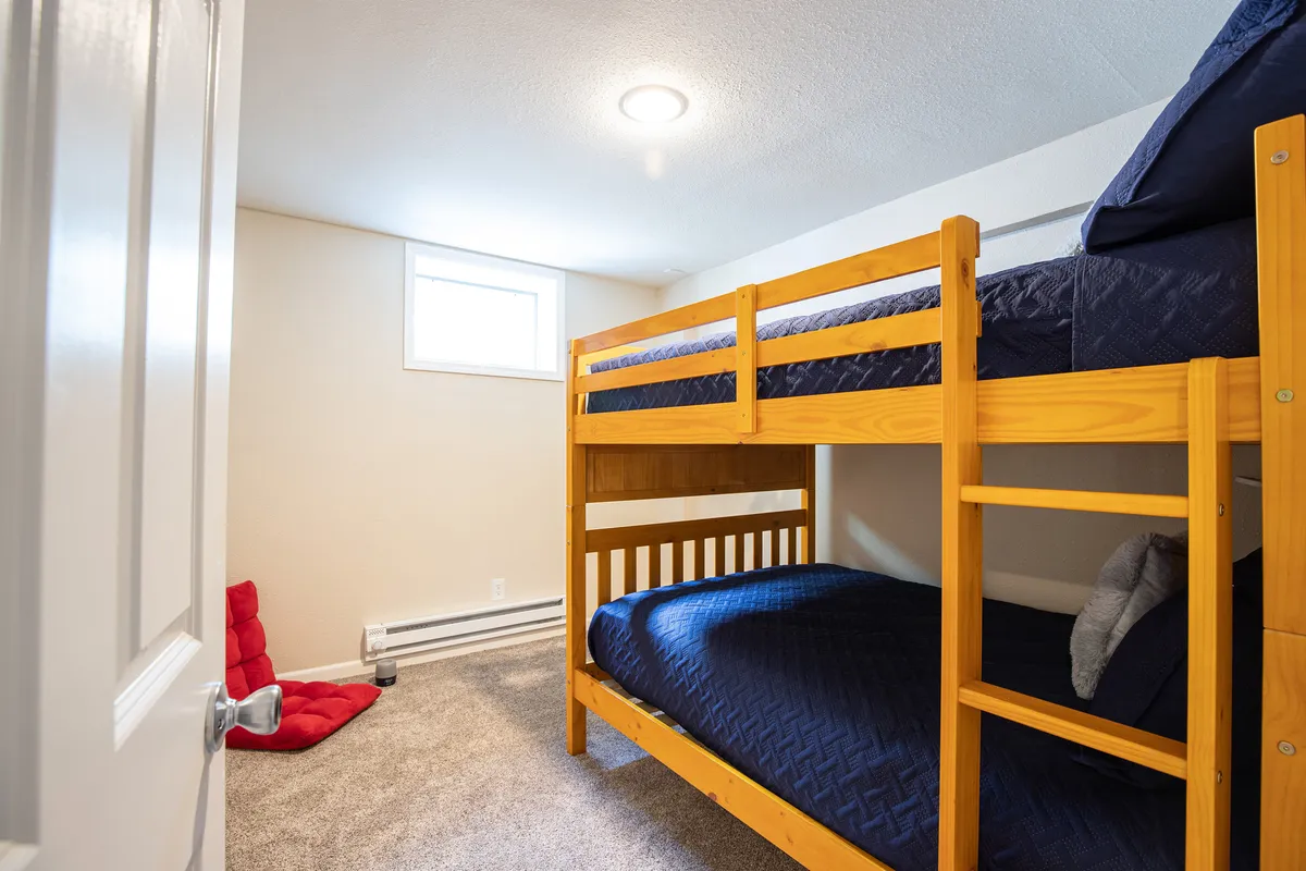 An inviting bunk room with multiple beds, a red bean bag chair, and a sunlit window. The playful and cozy atmosphere signals a perfect retreat for kids or teens within the twin-home setup, supporting the idea of everyone having their own space to relax.