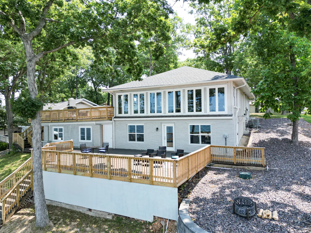 A wide wooden deck overlooks lush trees, with large windows connecting the outdoor living space to the house. The deck is surrounded by nature, providing an inviting spot for relaxing, outdoor dining, or spending time with pets. The scene emphasizes the transition between indoor comfort and outdoor adventure.