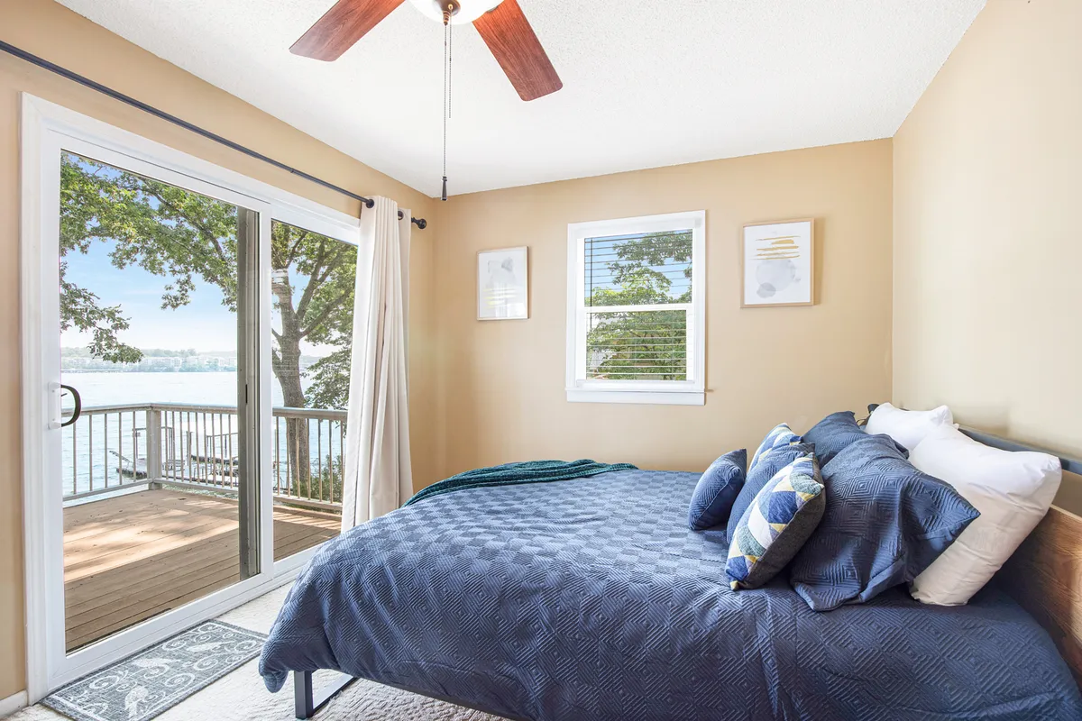 A serene bedroom with a large bed adorned with decorative pillows, an inviting seating area, and a sliding glass door that opens to beautiful water views. Tasteful wall art adds a touch of personality and warmth.