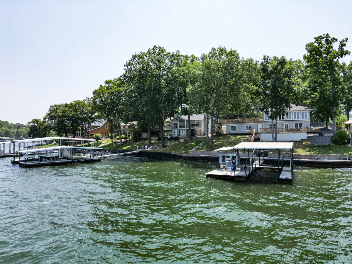 A tranquil lakefront scene featuring several properties with docks stretching into the water, lined by a gentle tree line. The calm water and expansive lakeside area create an inviting environment for strolls, water activities, or relaxing with pets.