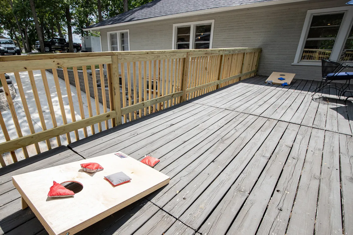 A playful scene on the deck features a cornhole board and red bean bags with deck railing in the background, conveying a lively, social mood.
