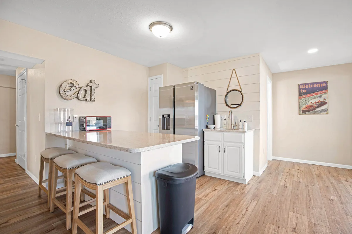 A stylish kitchen scene featuring a large island with barstools, a stainless steel refrigerator, and decorative wall art. The setup invites socializing, casual dining, and group meal preparation.