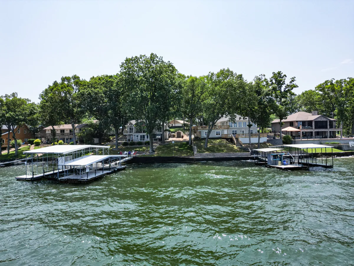 A relaxed waterfront view showing several lakefront homes, dock structures, and lush greenery. The image captures families enjoying boating, fishing, and water sports, set against a peaceful lakeside backdrop.