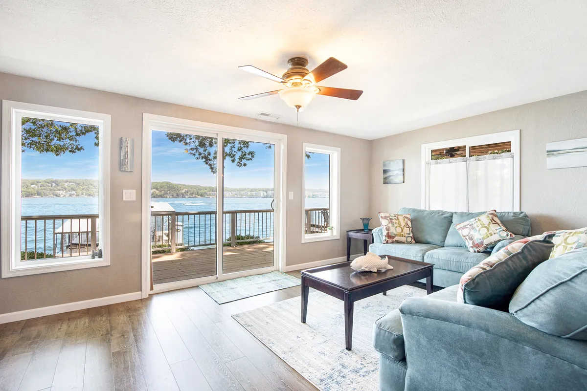 A tranquil and cozy living room with a comfortable sofa positioned to overlook large windows that frame a beautiful water view. A coffee table with decorative items adds a homey touch, making it an ideal space for relaxing, conversing, or simply enjoying the sunset over the lake.