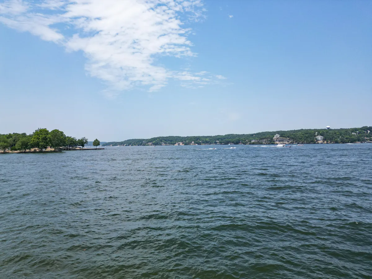 A sweeping view of the lake with expansive water, distant green hills, and small tree-covered islands under a picturesque sky. The image radiates tranquility and the spirit of outdoor adventure, perfect for boating, swimming, and relaxing on the shore.