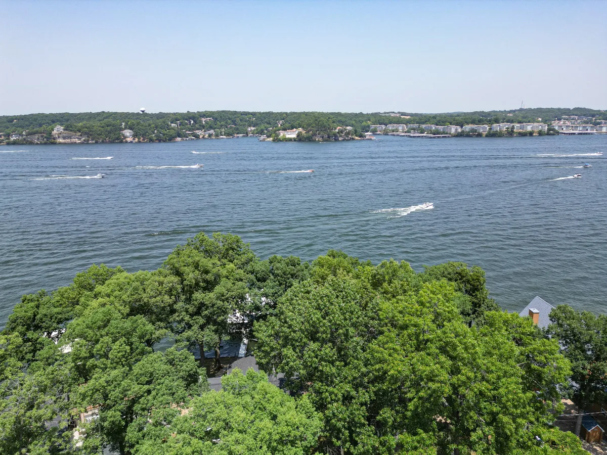 A broad, inviting view of the lake with expansive water, lush greenery along the shore, and visible boating activity. The image captures the excitement and serenity of the Lake of the Ozarks, making it an ideal visual for exploration and excursions.